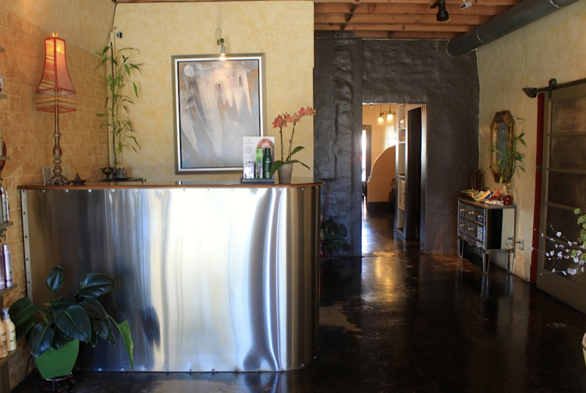 Modern salon reception area with sleek metal counter and cozy decor, promoting professional beauty services.
